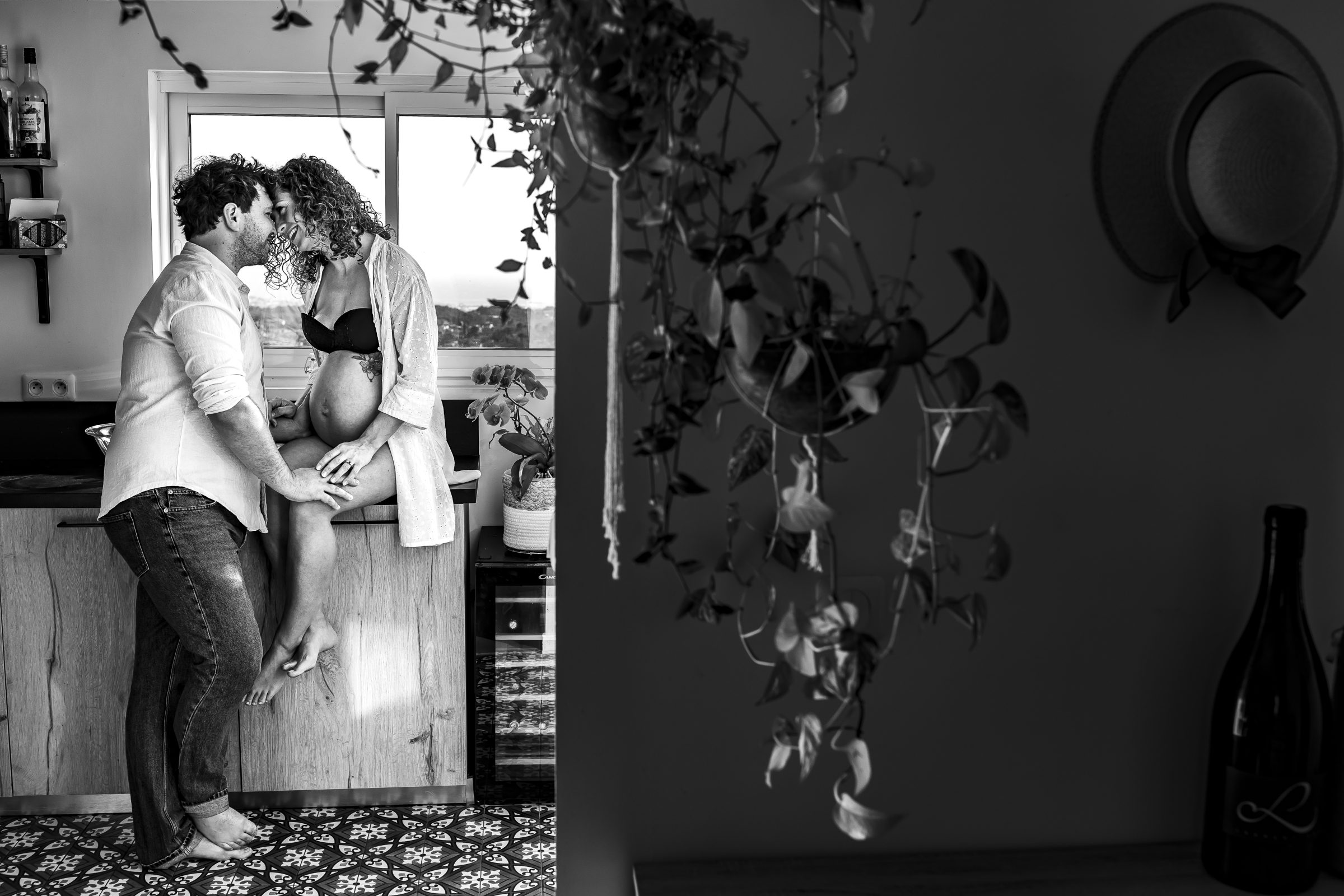 un couple d amoureux qui se serrent 'un contre l'autre , elle est assise sur le plan de travail avec son ventre rond de femme enceinte, ils sont front contre front sur une belle photo en noir et blanc